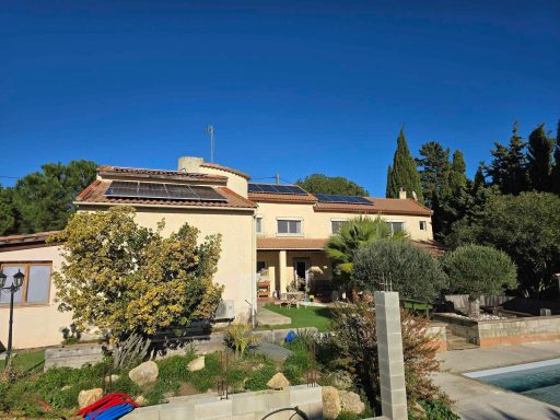 Maison avec panneaux solaires, piscine et jardin, sous un ciel dégagé.