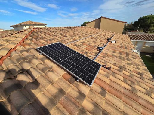 Panneau solaire installé sur un toit en tuiles, ciel partiellement nuageux en arrière-plan.