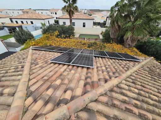 Panneaux solaires installés sur un toit avec des maisons et de la végétation en arrière-plan.