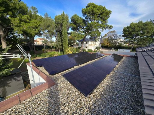 Panneaux solaires sur un toit, avec des arbres et un jardin en arrière-plan.