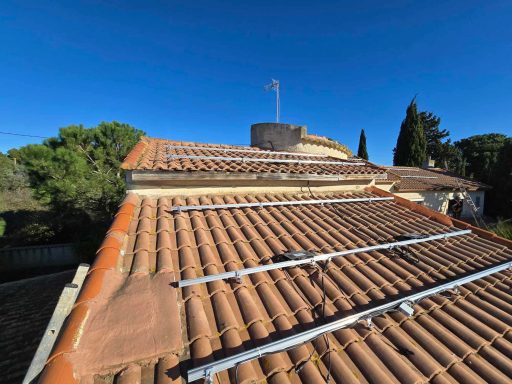 Toit en tuiles avec panneaux solaires sous un ciel bleu, entouré d'arbres.