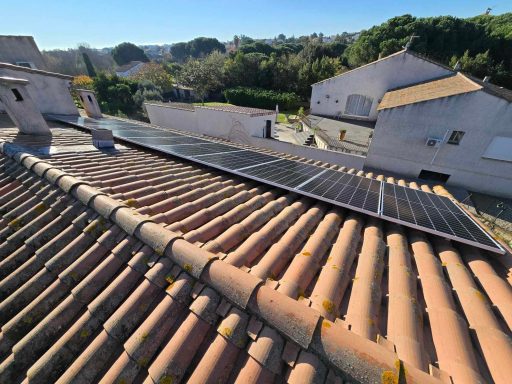 Panneaux solaires sur un toit en tuiles, paysage verdoyant en arrière-plan.